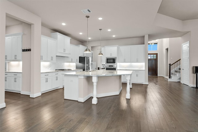 kitchen featuring white cabinetry, appliances with stainless steel finishes, a center island with sink, and hanging light fixtures