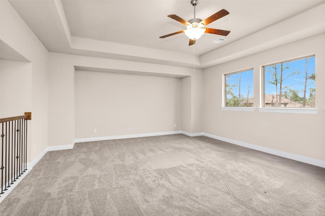 empty room with ceiling fan, a raised ceiling, and light carpet