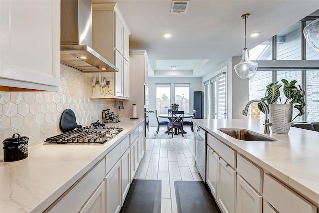 kitchen featuring wall chimney range hood, sink, hanging light fixtures, light stone countertops, and decorative backsplash