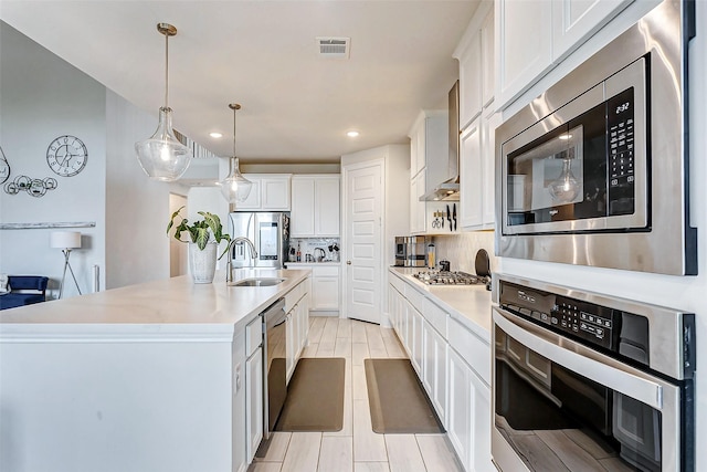 kitchen featuring sink, appliances with stainless steel finishes, a kitchen island with sink, white cabinetry, and tasteful backsplash