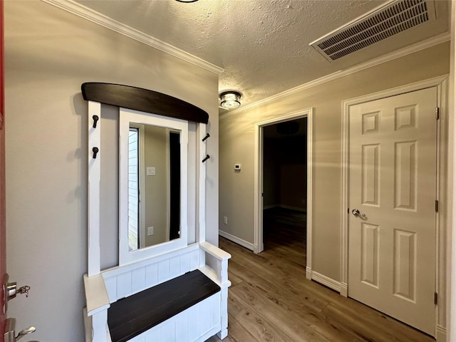interior space with a textured ceiling, visible vents, baseboards, ornamental molding, and wood finished floors