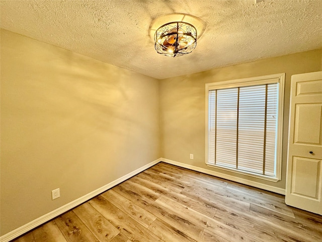 spare room with a textured ceiling, wood finished floors, and baseboards