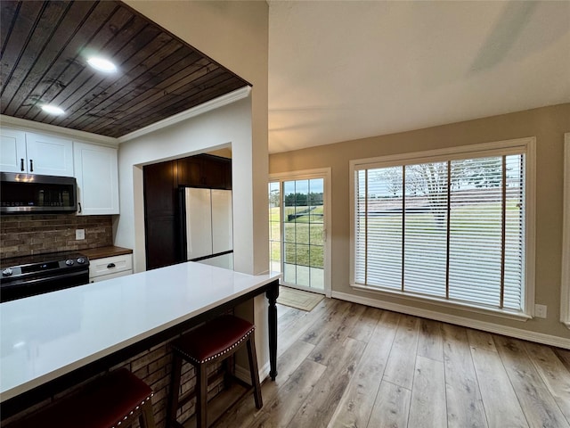 kitchen featuring black range with electric stovetop, stainless steel microwave, tasteful backsplash, white cabinets, and a kitchen bar