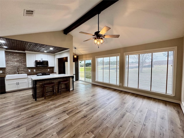 kitchen with stainless steel microwave, a sink, decorative backsplash, white cabinetry, and open floor plan