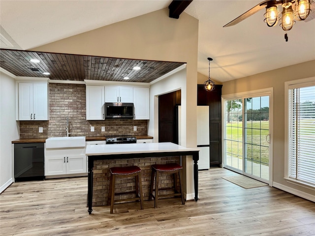 kitchen with lofted ceiling with beams, appliances with stainless steel finishes, white cabinets, a sink, and a ceiling fan