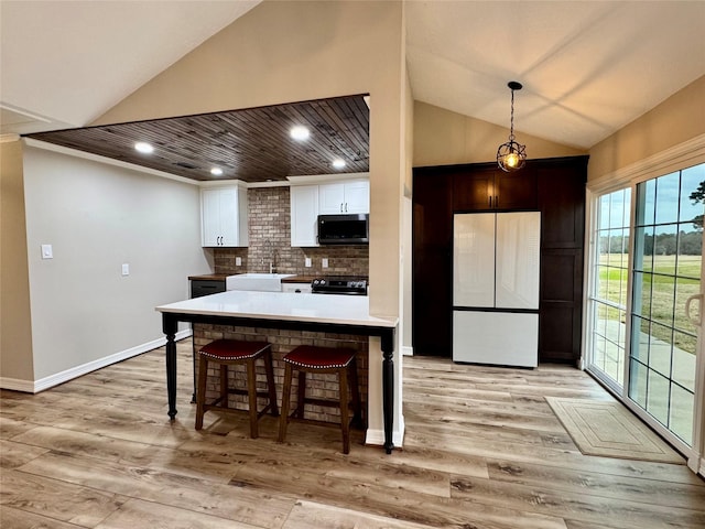 kitchen featuring lofted ceiling, stainless steel microwave, white cabinetry, freestanding refrigerator, and electric stove