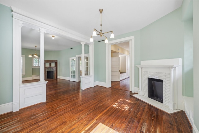 unfurnished living room with a brick fireplace, dark wood-type flooring, decorative columns, and a chandelier