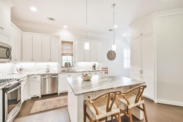 kitchen with decorative light fixtures, white cabinets, a center island, and appliances with stainless steel finishes