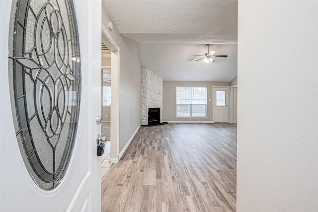 unfurnished living room featuring light hardwood / wood-style floors, a fireplace, a textured ceiling, ceiling fan, and lofted ceiling