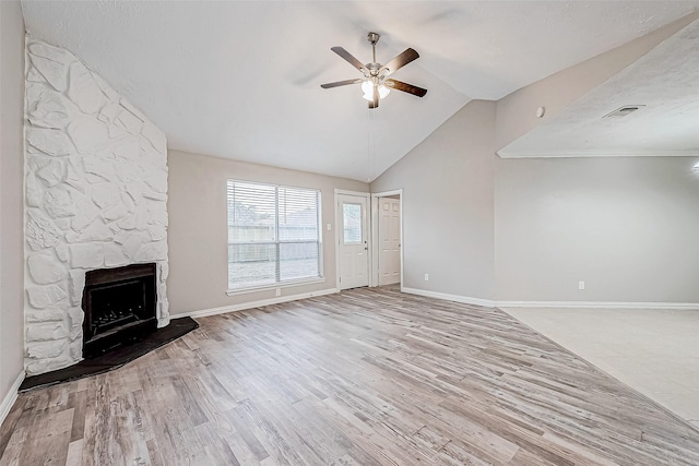 unfurnished living room featuring light wood-type flooring, vaulted ceiling, a stone fireplace, and ceiling fan