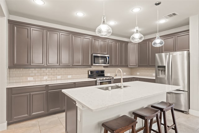 kitchen featuring sink, a kitchen island with sink, hanging light fixtures, stainless steel appliances, and light stone countertops