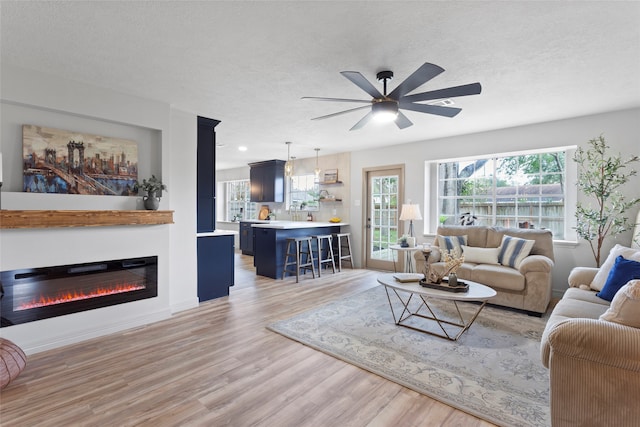 living room featuring ceiling fan, light hardwood / wood-style flooring, and a textured ceiling