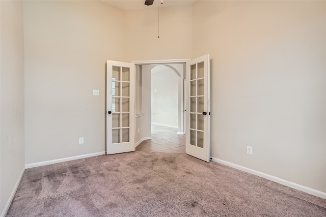 carpeted empty room with a towering ceiling, ceiling fan, and french doors