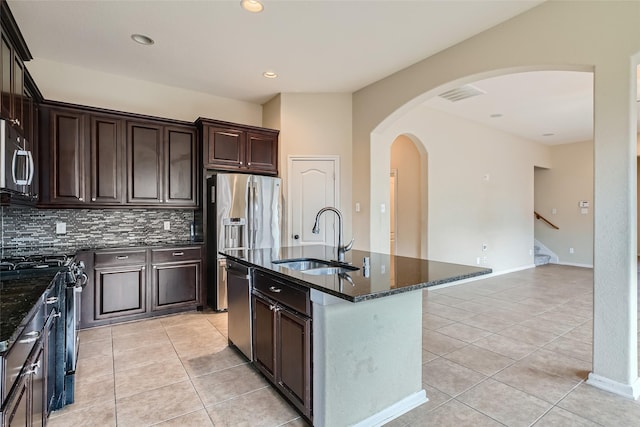 kitchen with appliances with stainless steel finishes, light tile patterned floors, sink, backsplash, and a center island with sink