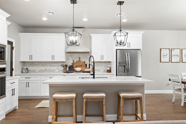 kitchen with decorative light fixtures, sink, white cabinetry, a kitchen island with sink, and stainless steel appliances