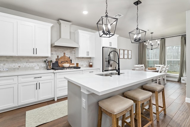 kitchen with premium range hood, an island with sink, white cabinets, and a breakfast bar