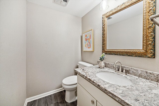 bathroom with toilet, wood finished floors, vanity, visible vents, and baseboards