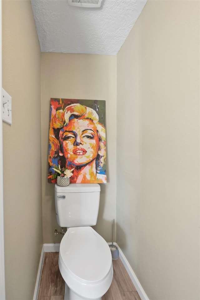 bathroom with wood-type flooring, toilet, and a textured ceiling