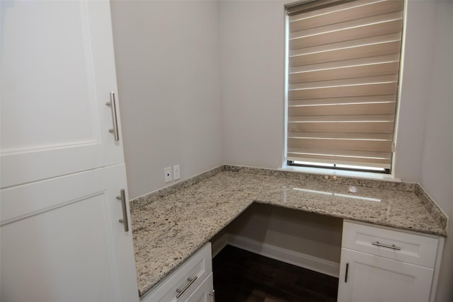 kitchen with white cabinets, built in desk, dark hardwood / wood-style floors, and light stone countertops