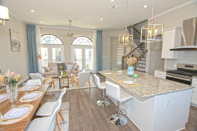 kitchen with light stone countertops, white cabinets, french doors, stainless steel gas stove, and wall chimney exhaust hood