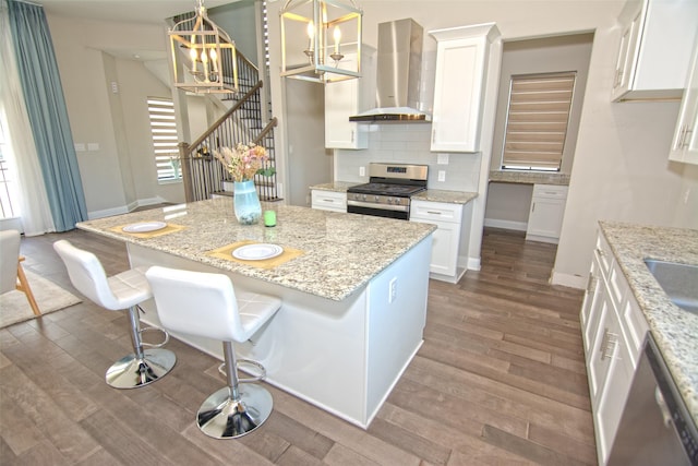 kitchen with hanging light fixtures, white cabinets, light stone countertops, ventilation hood, and stainless steel appliances