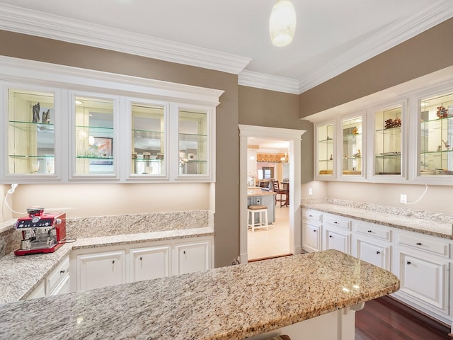 kitchen featuring white cabinets, decorative light fixtures, dark hardwood / wood-style flooring, light stone counters, and crown molding