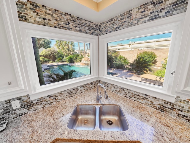 interior details with sink, backsplash, white cabinets, and light stone counters