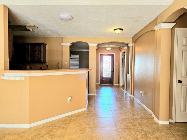 kitchen with dark brown cabinets, decorative columns, a textured ceiling, and light tile patterned floors