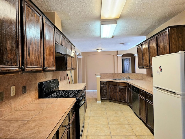 kitchen with light tile patterned floors, white fridge, dark brown cabinetry, dishwashing machine, and black range with gas stovetop