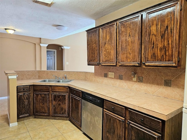 kitchen with a textured ceiling, light tile patterned floors, stainless steel dishwasher, sink, and kitchen peninsula