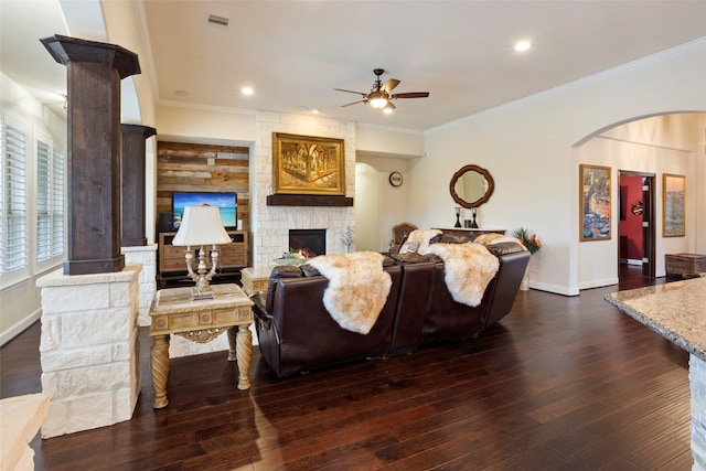 living room with crown molding, dark wood-type flooring, ceiling fan, and a stone fireplace