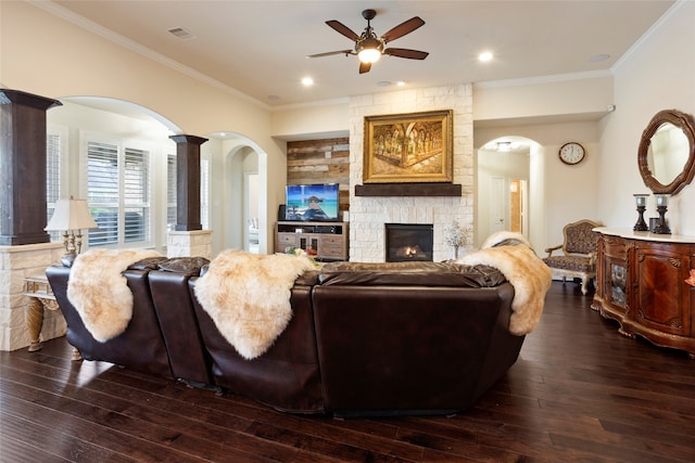 living room with crown molding, ceiling fan, a stone fireplace, and dark hardwood / wood-style flooring