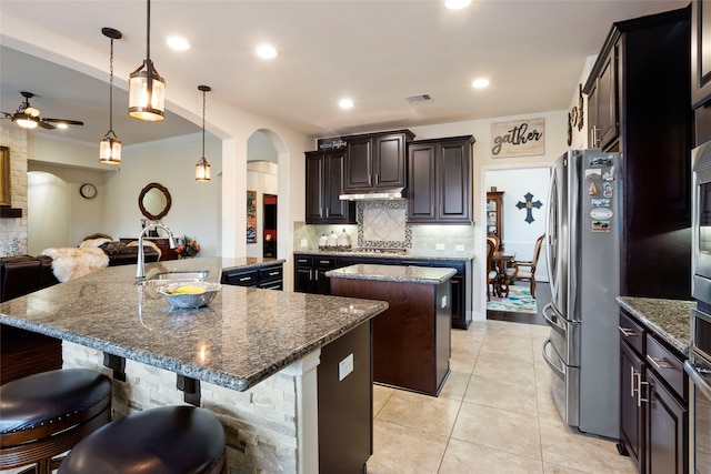 kitchen with appliances with stainless steel finishes, hanging light fixtures, a kitchen island with sink, a kitchen breakfast bar, and sink