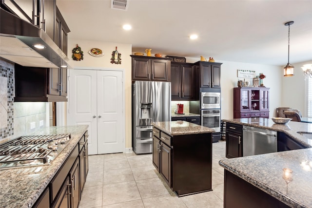 kitchen with light stone countertops, appliances with stainless steel finishes, a center island, decorative backsplash, and hanging light fixtures