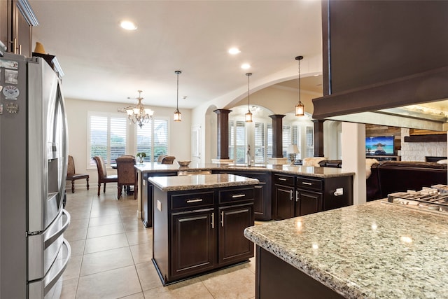 kitchen with light stone countertops, a kitchen island, stainless steel refrigerator with ice dispenser, decorative light fixtures, and dark brown cabinets