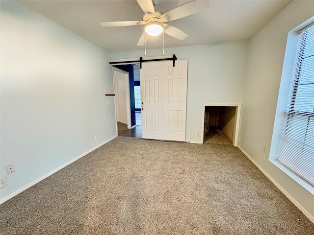 unfurnished bedroom with multiple windows, ceiling fan, a barn door, and carpet flooring