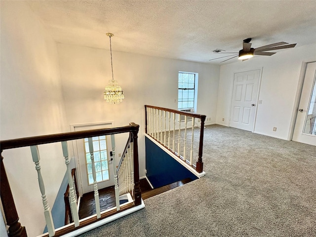 staircase featuring carpet flooring, ceiling fan with notable chandelier, and a textured ceiling