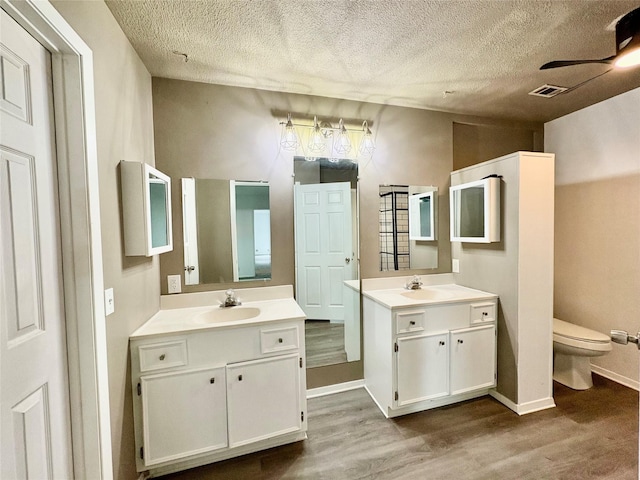 bathroom with wood-type flooring, toilet, vanity, and a textured ceiling