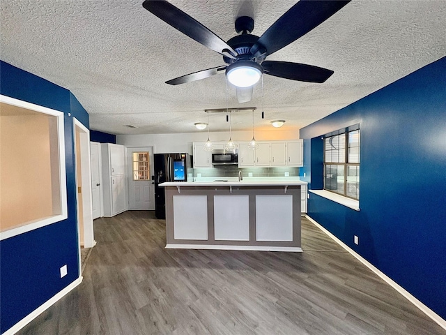 kitchen featuring pendant lighting, white cabinetry, hardwood / wood-style flooring, a center island, and black fridge