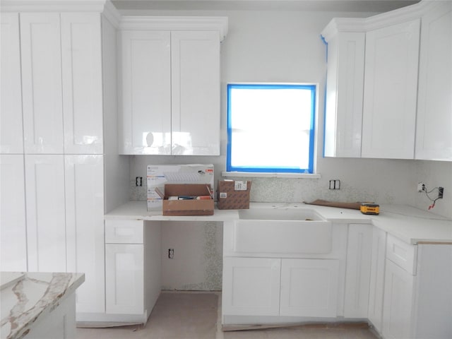 kitchen featuring light stone countertops, white cabinets, and sink