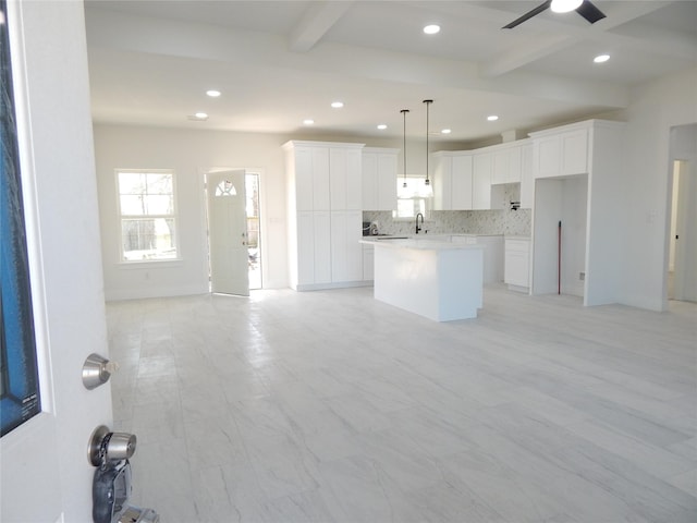 kitchen featuring a kitchen island, white cabinetry, light countertops, hanging light fixtures, and beam ceiling