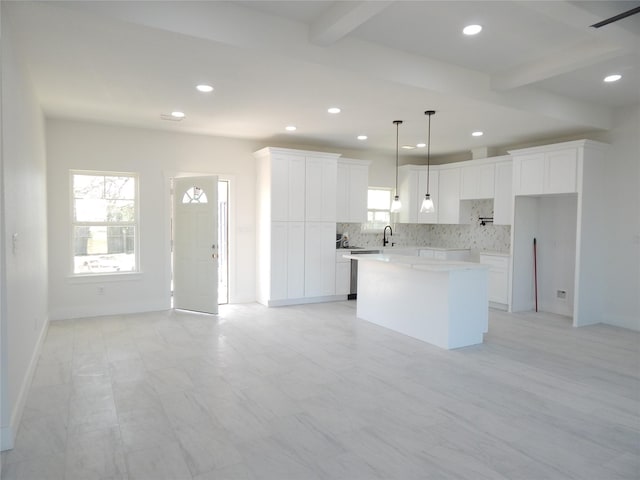 kitchen with white cabinets, light countertops, beam ceiling, a center island, and decorative light fixtures