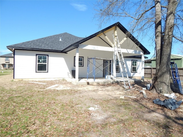 rear view of house featuring a shingled roof and fence