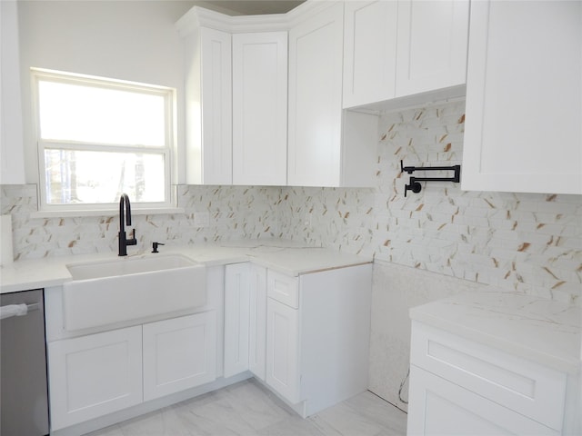 kitchen with stainless steel dishwasher, a sink, white cabinetry, and light stone countertops