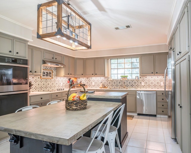 kitchen featuring crown molding, light tile patterned floors, an island with sink, stainless steel appliances, and a breakfast bar area