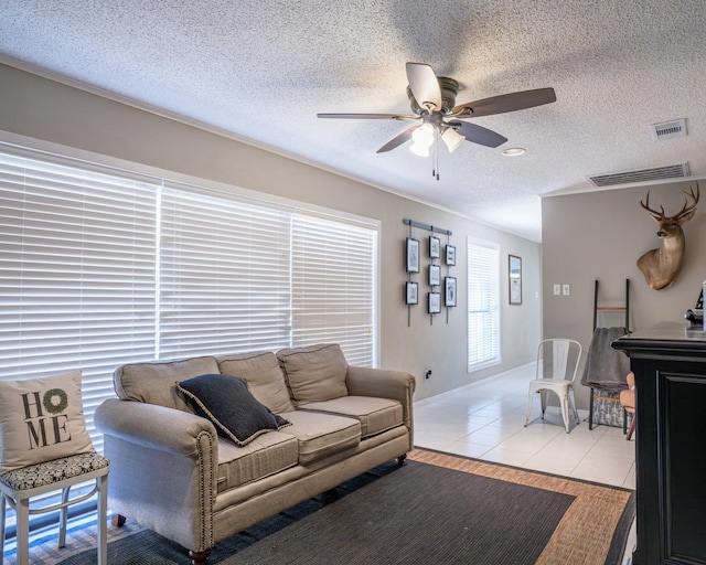 tiled living room with a textured ceiling, ceiling fan, and ornamental molding