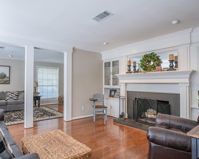 living room featuring decorative columns, crown molding, a fireplace, and wood-type flooring