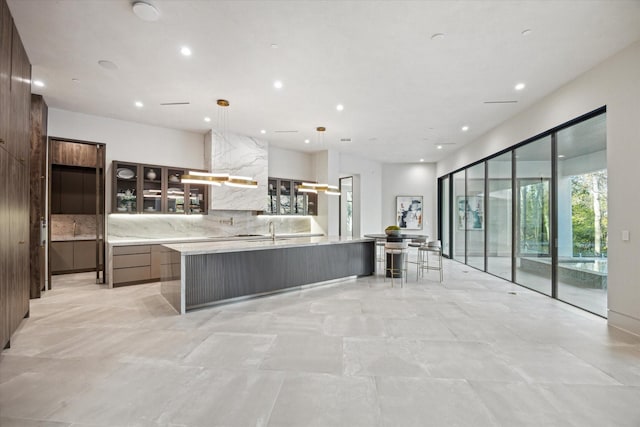 kitchen with tasteful backsplash, a spacious island, hanging light fixtures, dark brown cabinets, and sink