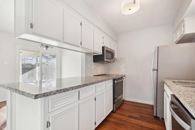 kitchen featuring light stone countertops, white cabinets, dark hardwood / wood-style flooring, stainless steel appliances, and kitchen peninsula