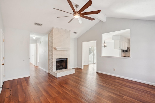 unfurnished living room with ceiling fan with notable chandelier, vaulted ceiling with beams, dark hardwood / wood-style floors, and a fireplace